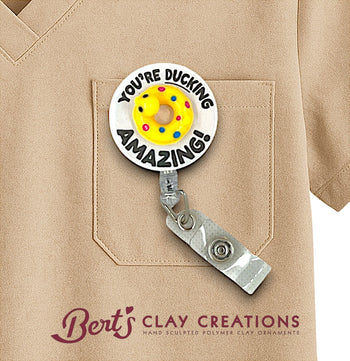 Badge holder with 'You're Ducking Amazing!' text and colorful design on a beige shirt pocket, featuring Bert's Clay Creations branding.